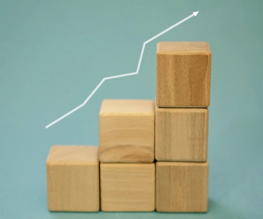 Photo of wooden building blocks stacked on top of each other against a blue background with a white arrow up and to the right.